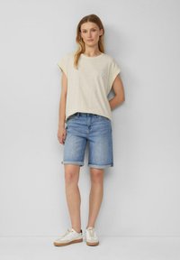 Lichtbeige, losvallend T-shirt met opgerolde mouwen en een kleine blauwe ster geborduurd. Gecombineerd met denim shorts en witte sneakers.