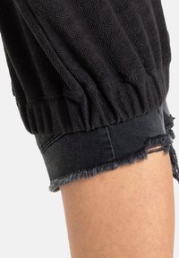 Black textured fabric with a herringbone pattern, featuring gathered elastic cuffs and distressed denim with frayed edges.
