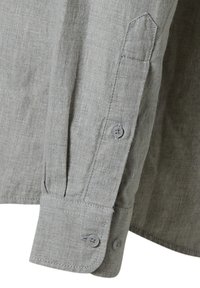 Maglietta grigia a maniche lunghe in tessuto texture, con polsini abbottonati e colletto leggermente a punta. Due bottoni sul polsino della manica.