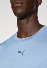 Lichtblauwe sporttanktop met een gladde textuur, ronde halslijn en een donkerblauw Puma-logo op de borst.