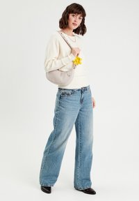 Creme sweater, lyseblå vide jeans, sorte spidse sko og en grå taske med en gul blomst detalje. Enkel kædedesignhalskæde inkluderet.