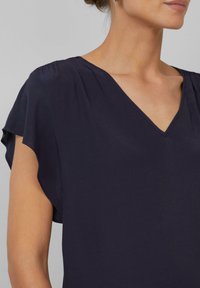 Haut bleu marine à manches courtes avec un décolleté en V. Tissu doux, coupe ample avec un détail froncé aux épaules, texture lisse, détails minimalistes.