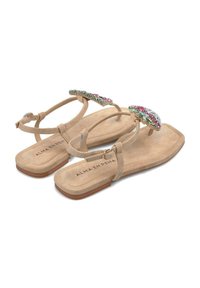 Sandali piatti in suede beige con intricate decorazioni in gemme sul cinturino, caratterizzati da un design a punta rotonda e cinturino alla caviglia regolabile.