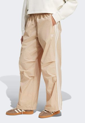 Pantaloni da tuta beige, leggeri e morbidi, con vita elasticizzata, caratterizzati da tre strisce bianche sui lati e tasche laterali.