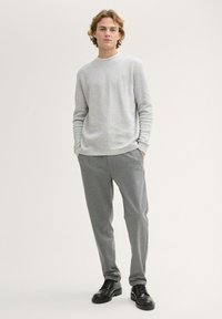 Hellgrau geripptes Langarmshirt, kombiniert mit dunkelgrauen schmal geschnittenen Hosen. Modell trägt schwarze Schnürschuhe. Neutrale Hintergrund.