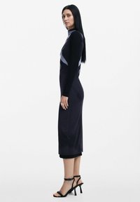 Rochie lungă, mulată, de culoare neagră, cu guler înalt, având elemente de design contrastante de culoare gri. Modelul poartă sandale negre cu toc subțire. Textură netedă.