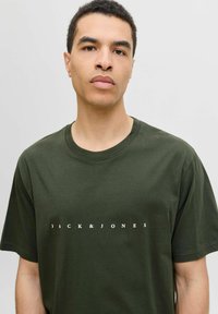 Roheline puuvillane T-särk lühikeste varrukatega, millel on ümmargune kaelus ja valge trükitud "JACK & JONES" logo rinna piirkonnas.