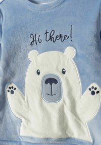 Cămașă din fleece albastru, decorată cu un urs brodat alb, cu o față zâmbitoare, lăbuțe în val și textul "Bună ziua!" în albastru închis.