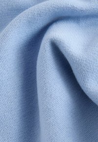 Vaaleansininen neulottu kangas, jossa on sileä pinta, hienot ja tasaiset ompeleet, tiheästi kudottu kestävyys ja lämpöä varten.