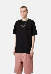 Camiseta de algodón negra con un diseño en forma de corazón en el pecho. Acompañada de pantalones cortos de mezclilla rosas, que exhiben un corte relajado y un estilo casual.