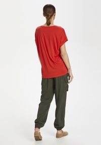 Red short-sleeve t-shirt with a loose fit, paired with olive cargo pants featuring elastic cuffs, and beige slip-on shoes.