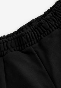 Schwarze Sweatpants mit einem elastischen Bund, der eine gerippte Textur aufweist. Hergestellt aus weichem Stoff, der entlang der Nähte sichtbare Steppnähte zeigt.