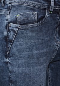 Jeans de denim azul oscuro con un clásico diseño de cinco bolsillos, un ligero desgaste y costuras reforzadas a lo largo de las costuras.