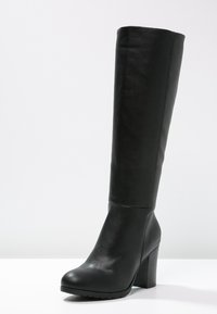 Botte noire en cuir jusqu'au genou, au design épuré, bout arrondi, talon bloc haut et surface texturée. Sans éléments métalliques visibles ni motifs.