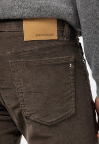 Bruna manchesterbyxor med en läderbakficka med präglat varumärke. Inkluderar två bakfickor med söm detaljer.