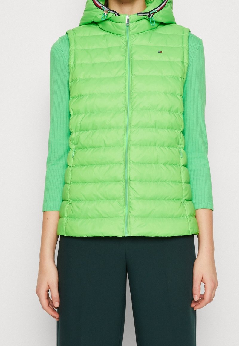 Gilet puffer verde con cappuccio, con chiusura a zip frontale e tasche laterali. Realizzato in materiale leggero con un design trapuntato e bordo a contrasto.