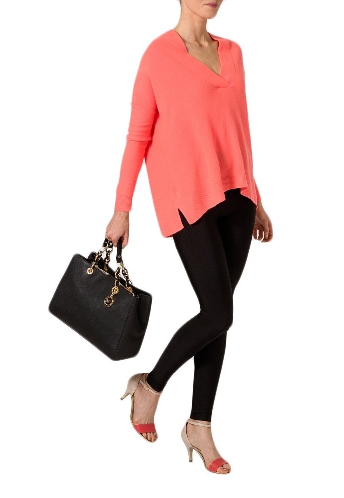 Maglione a V in corallo, leggings neri e tacchi beige con cinturini rossi. Modella che tiene una borsa nera con accessori dorati.