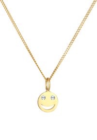 Guldhalskæde med en cirkulær smiley-ansigt vedhæng med to klare krystaller som øjne, hængende på en delikat kæde.