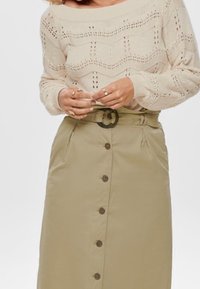 Pull en tricot crème avec un motif ondulé, associé à une jupe kaki à boutons sur le devant et à taille ceinturée.