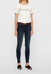 Camiseta blanca con el texto "Forever", vaqueros ajustados azules, cinturón marrón y sandalias negras tipo slide. Tela suave, ajuste casual y diseño simple.