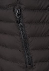 Svart puffjacka i tyg med en diagonalt dragkedja. Texturerad yta med kviltade sektioner som visar en strömlinjeformad design och robusta detaljer.