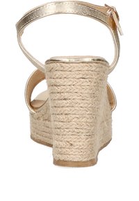 Sandalia de cuña con una correa metálica dorada en el tobillo, tacón de yute beige texturizado, diseño de talón abierto y suela interna suave.