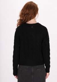 Schwarzer Strickpullover mit langen Ärmeln und rundem Halsausschnitt. Strukturierter Stoff und gerippter Saum. Keine sichtbaren Logos oder Muster.
