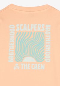 Brzoskwiniowa bawełniana bluza crewneck z odważnym graficznym tekstem w kolorze turkusowym i białym oraz wzorem promieni słonecznych z akcentami czaszki.