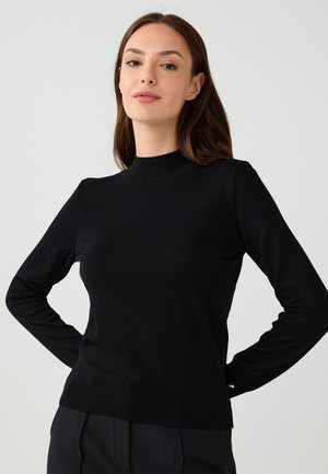 Pull noir à manches longues avec un col montant, des poignets et un ourlet côtelés. Fait en un matériau doux et extensible. Design minimaliste sans motifs.
