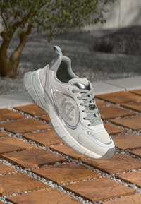 Világosszürke sportcipő hálós panelekkel, ezüst díszítéssel és texturált talppal. Fűzőkkel és az oldalon látható logóval rendelkezik.