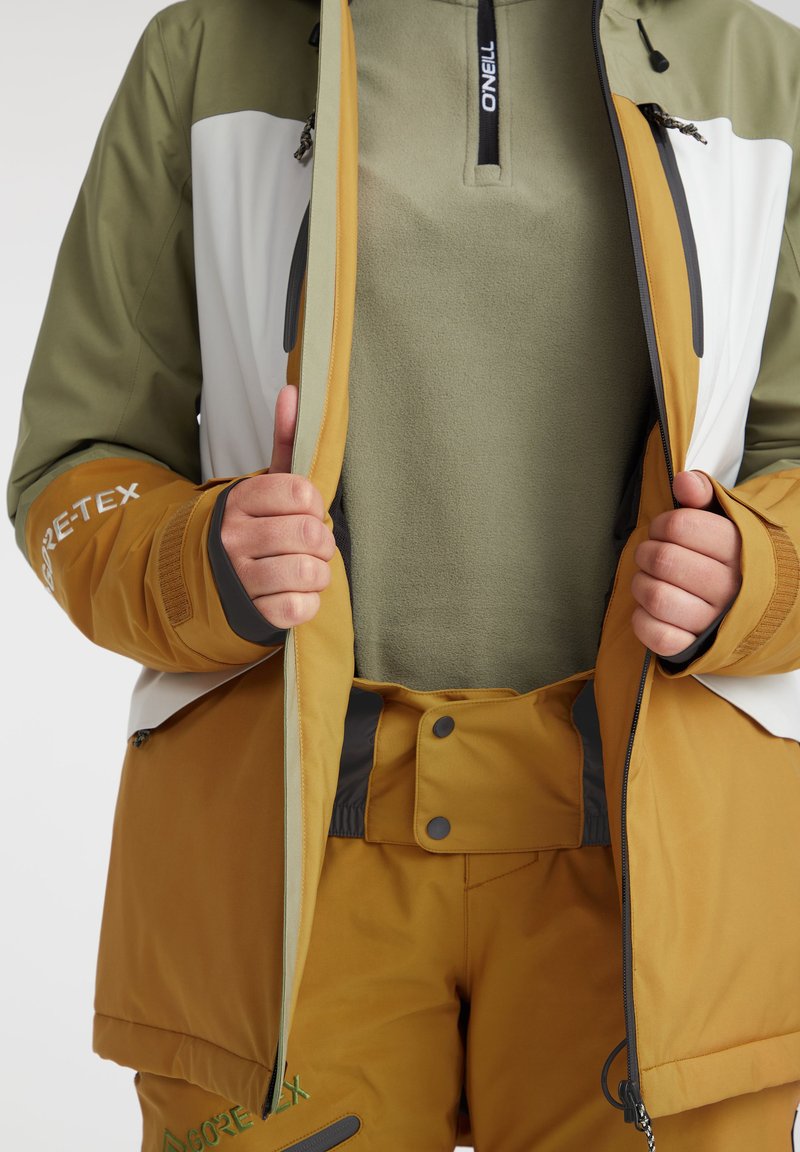 GORE-TEX-Jacke in Olivgrün, Weiß und Amber; verfügt über einen Reißverschluss vorne, Fleece-Futter, elastische Bündchen und verstellbare Säume. Passende Amber-Hosen.