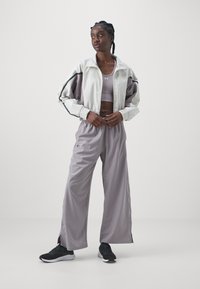 Light gray cropped jacket with elastic cuffs, paired with a matching sleeveless top and loose gray pants. Black athletic shoes complete the look.