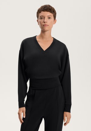 Black oversized V-neck sweater with long sleeves and ribbed waist. Soft texture and simple design, paired with matching black trousers.