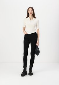 Krem farge kortermet polo skjorte, svarte høytlivde skinny jeans, svarte snørebånds militærstøvler, og en liten svart veske. Glatt stoff, tettsittende design.