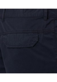 Marineblauwe stof, met één enkel opgestikte zak met een rechthoekige flap en gestikte details. Gladde textuur, casual ontwerp.