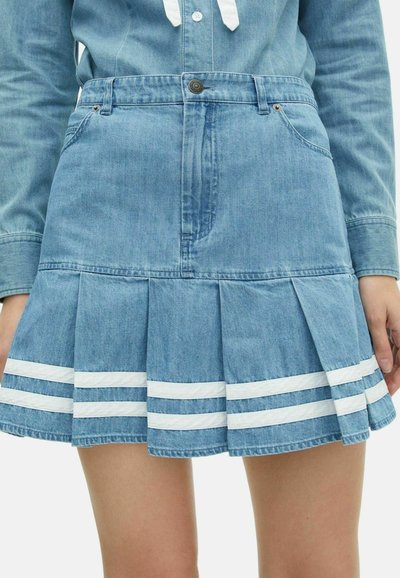 Lichtblauwe denim plissé rok met witte strepen aan de onderrand, gedragen met een bijpassend denim overhemd met knopen en lange mouwen.