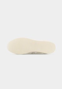 Σόλα παπουτσιού με συνεχόμενες παράλληλες αυλακώσεις που παρέχουν πρόσφυση, από εκρού καουτσούκ, εμφανιζόμενη επίπεδη πάνω σε ανοιχτό φόντο.