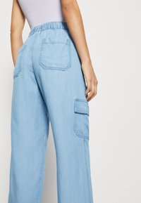 Jasnoniebieskie spodnie cargo z elastyczną talią, dwoma tylnymi kieszeniami oraz boczną kieszenią, charakteryzujące się gładką deniwową teksturą i szerokimi nogawkami.