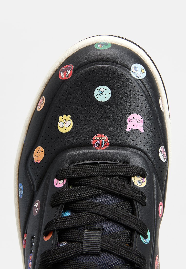 Sneakers en cuir noir dotés d'impressions colorées de visages de dessins animés, d'une surface texturée, de lacets noirs et d'une semelle en caoutchouc crème.