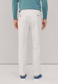 Witte broek met een slim fit, voorzien van dubbele achterzakken met bruine knopen, gestyled met een turquoise trui en blauwe schoenen.
