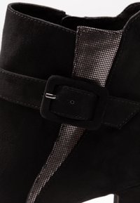 Zwarte suède enkellaars met een gestructureerde metalen strook en een riem met een rechthoekige gespsluiting. Glad oppervlak met een gestroomlijnd ontwerp.