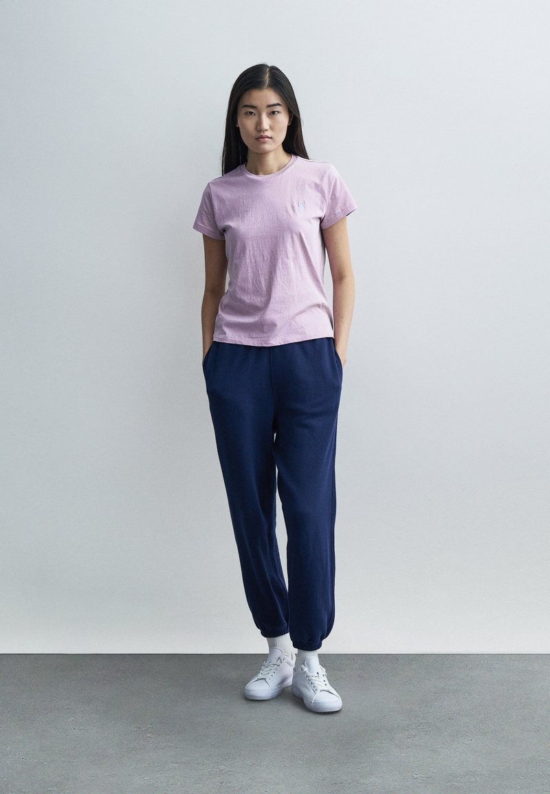 Ljuslila t-shirt med korta ärmar kombinerad med marinblå joggerbyxor. Outfitten har en avslappnad passform och modellen bär vita sneakers.