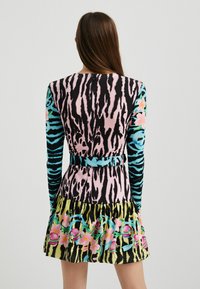 Robe colorée présentant un mélange de rayures zèbre noires et roses, manches longues, motifs floraux et une jupe évasée avec des accents vibrants.