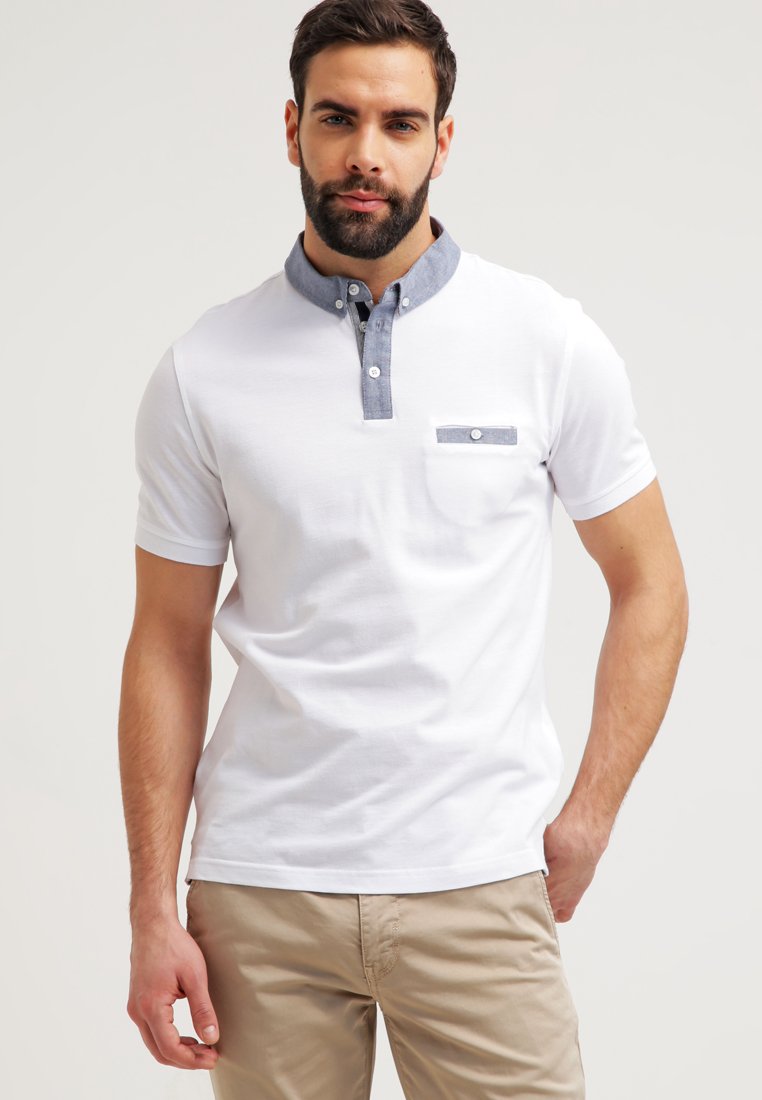 Hvit polo skjorte med grå krage og knappet brystlomme. Har en liten brystlomme med et horisontalt stripe-mønster. Laget av bomull.