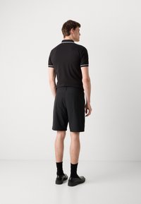 Svart polo skjorte med hvit kant, kombinert med svarte shorts. Personen har på seg svarte sokker og sko, sett fra ryggen.