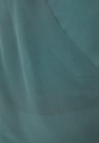 Türkiser Stoff mit einer glatten, leicht glänzenden Textur. Besitzt ein gefaltetes Design, das sanfte Kurven und subtile Farbnuancen schafft.