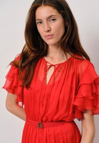 Rode chiffon jurk met gerimpelde mouwen, een striknek en een zijde riem met een gesp. Soepele textuur en vloeiende ontwerp.