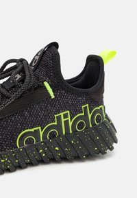 Černá sportovní bota s vrškem z síťoviny, jasně zelenými akcenty, výrazným logem "adidas" a texturovanou podešví se zelenými skvrnami.