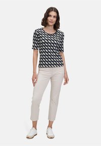 Donkerblauwe top met korte mouwen en een golfpatroon in crème, gecombineerd met lichtbeige broek en witte sneakers, staand voor een effen achtergrond.