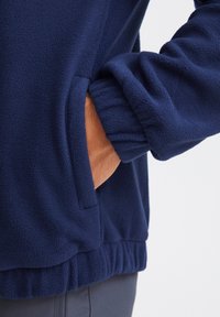 Giacca in fleece navy con finitura testurizzata, polsini elastici e tasca inserita sul lato per una maggiore funzionalità.